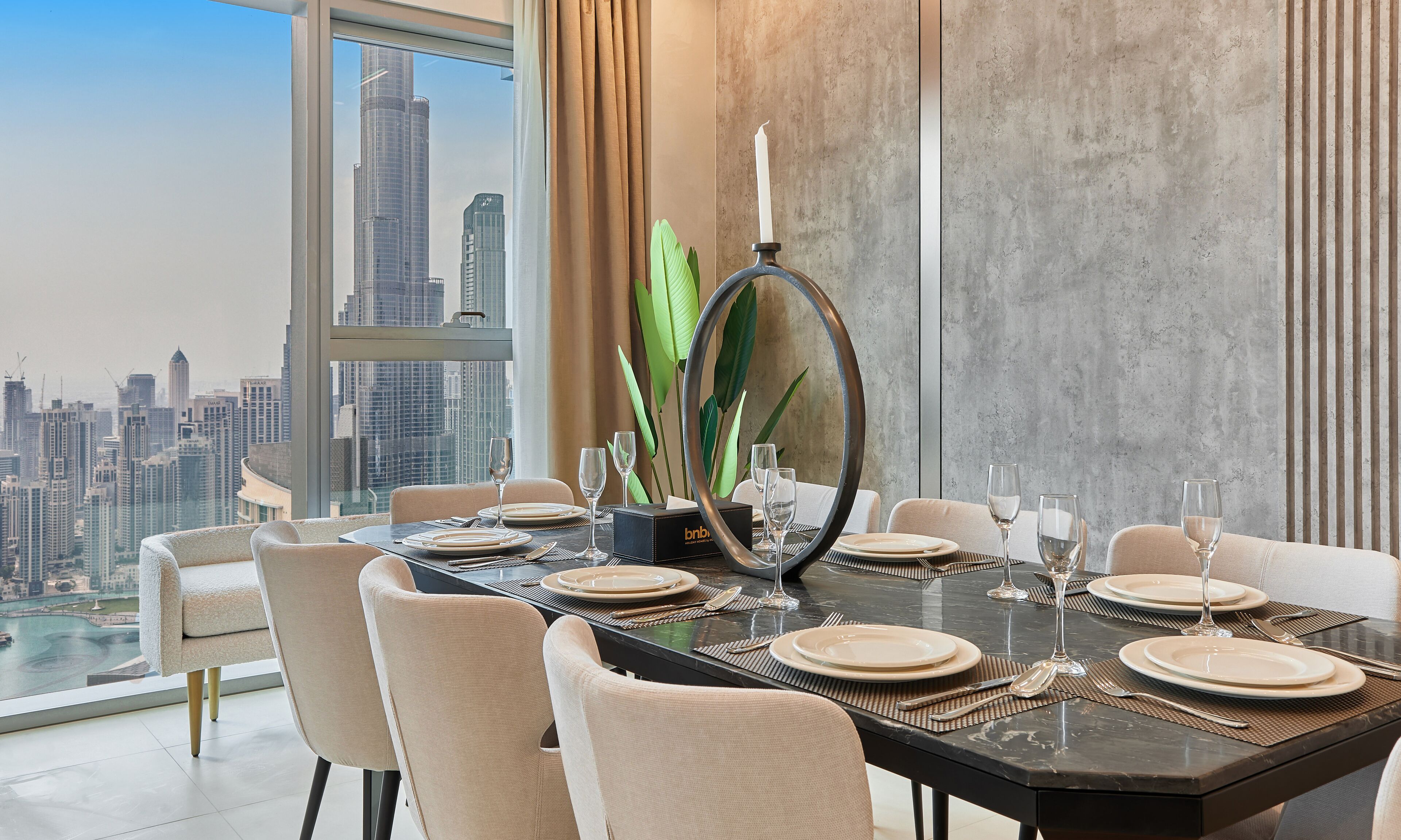 A dining area with a city view, a modern table set with plates and glasses, and a decorative mirror.
