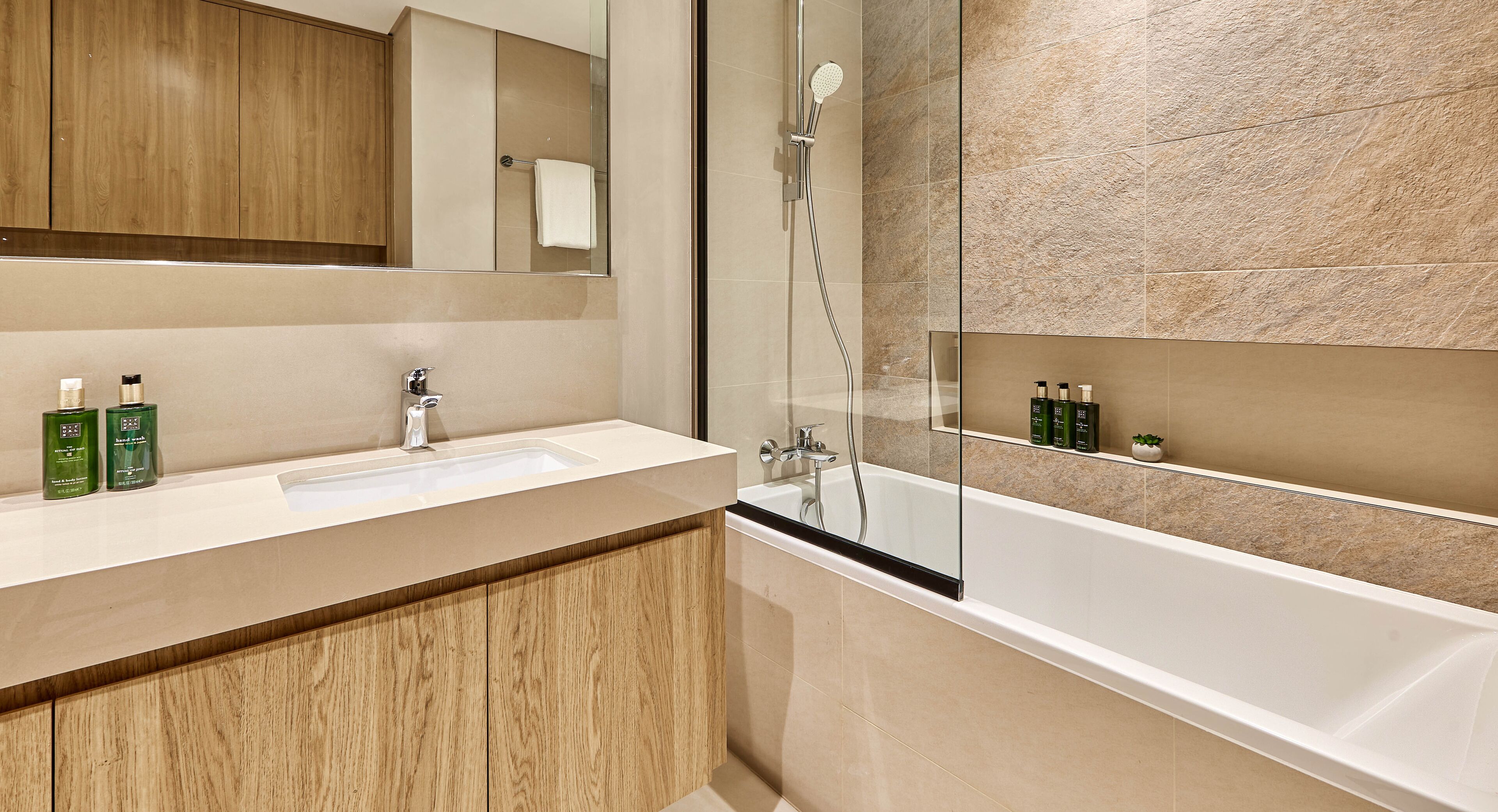 Ein modernes Badezimmer mit einem Holzkosmetikschrank, einem großen Spiegel, einem weißen Waschbecken und einer Badewanne.