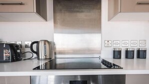 Una cocina moderna con una campana extractora de acero inoxidable, un hervidor y una cafetera. Hay tres enchufes en la pared y un recipiente para guardar café.