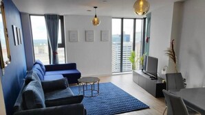 Una sala de estar moderna con un sofá azul, una mesa de centro, un televisor y un comedor.