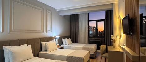 Ein Hotelzimmer mit zwei Betten, einem Schreibtisch, einem Fernseher und einem Fenster mit Blick auf die Stadt.