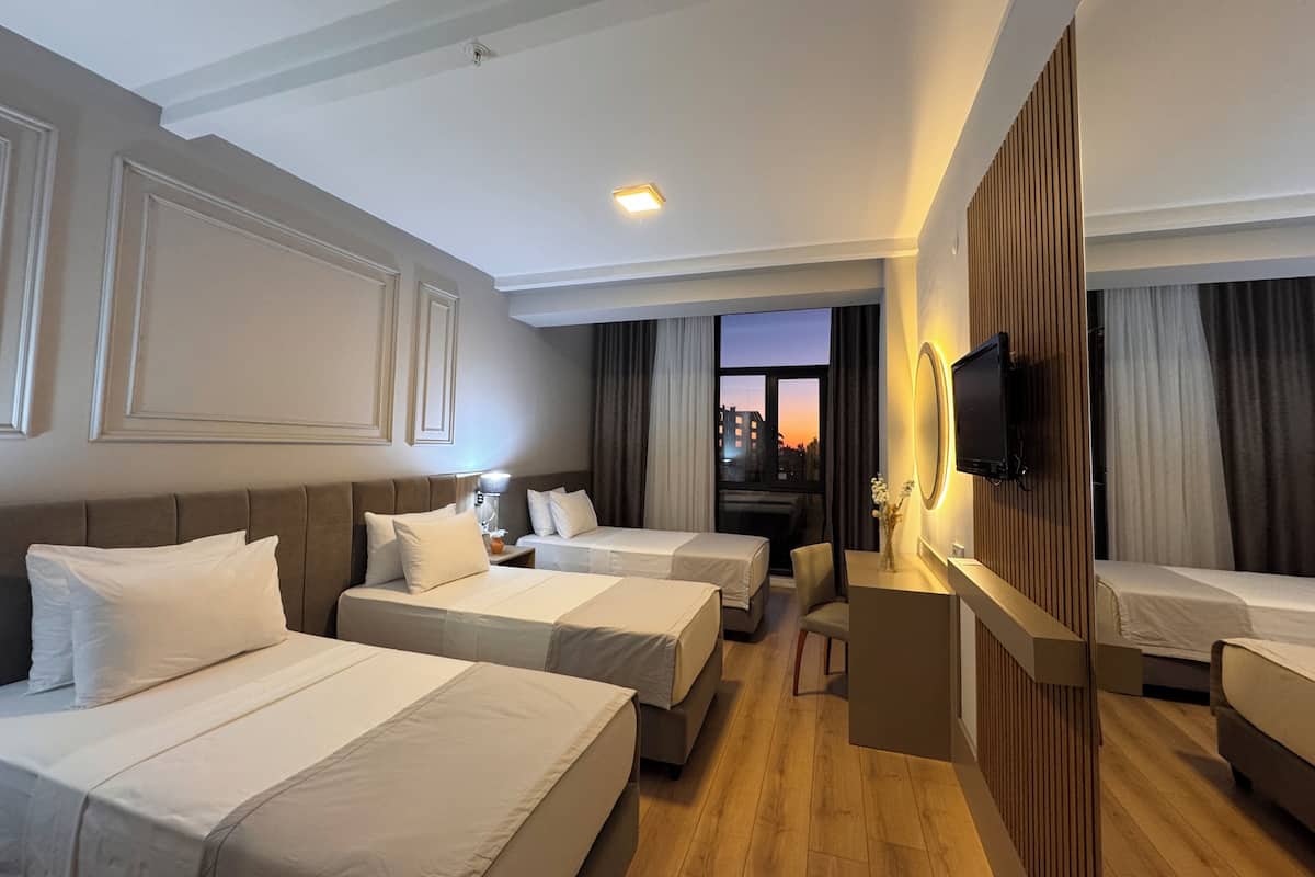 A hotel room with two single beds, a sofa, a TV, and a window with a view of buildings.