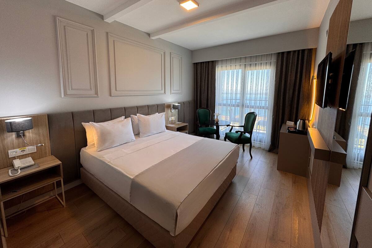 A hotel room with a large bed, bedside tables, a desk with a chair, a TV, and a window with curtains.