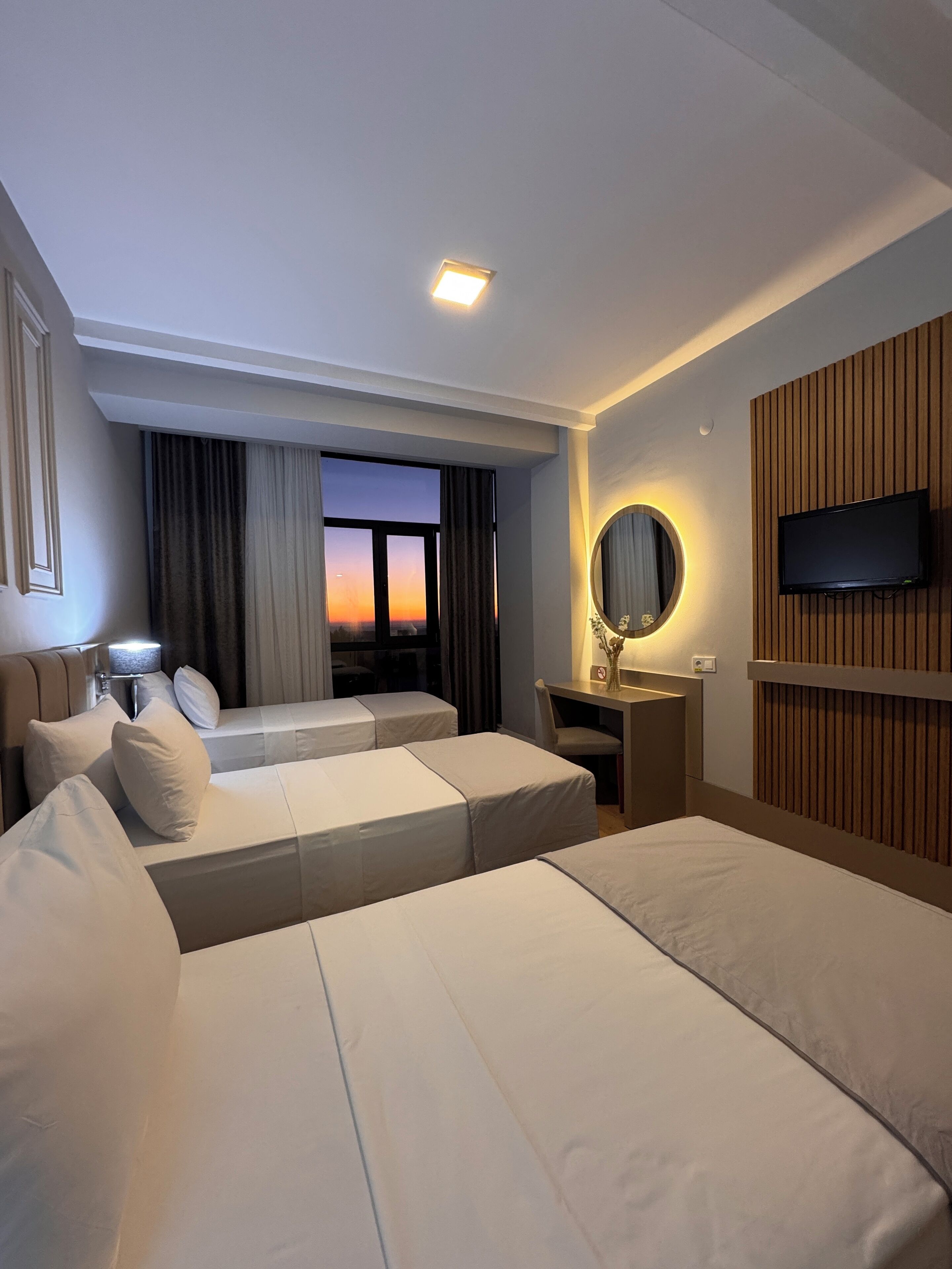 Habitación de hotel con dos camas, un escritorio, un televisor y vista al atardecer.