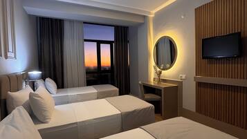 Habitación de hotel con dos camas, un escritorio, un televisor y vista al atardecer.