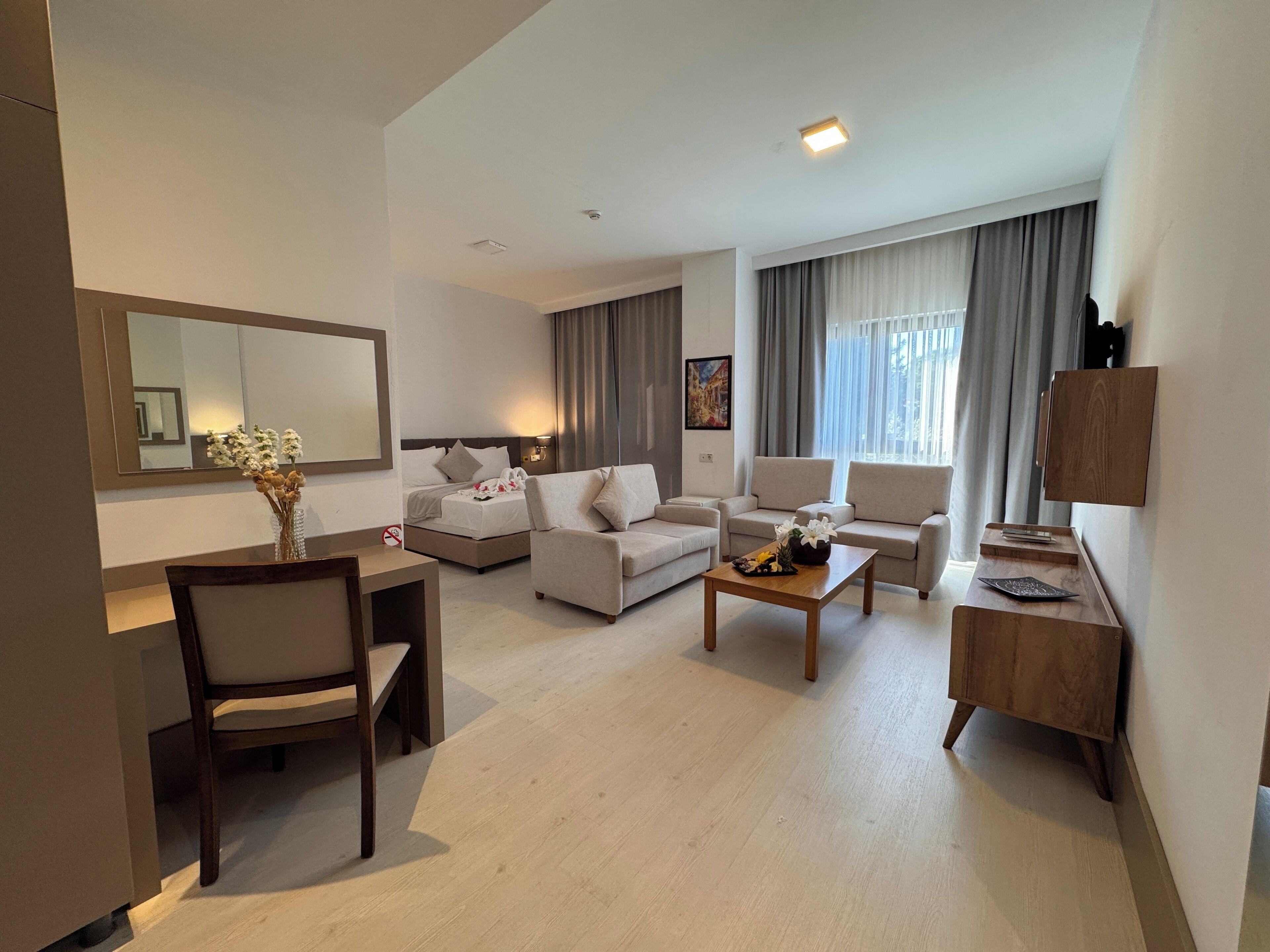 A modern hotel room with a bed, two sofas, a dining table, and a TV.