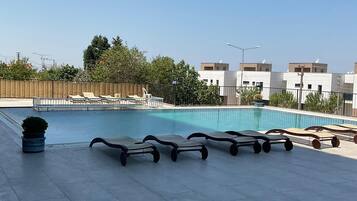 A rooftop swimming pool with lounge chairs and a trash bin.