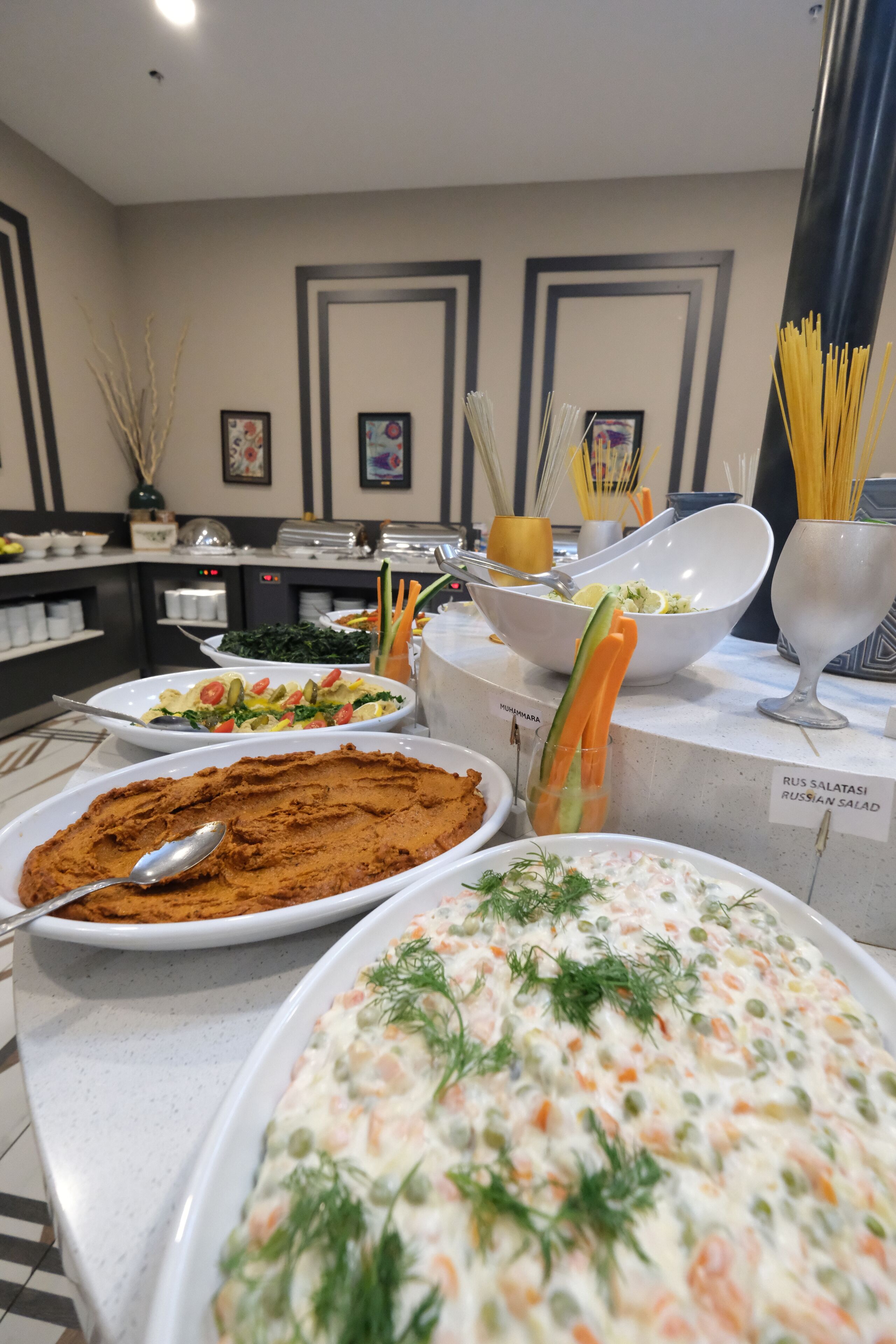 A buffet with various dishes including a Russian salad, a creamy salad, and a hummus dish.