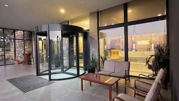 Un vestíbulo moderno con puerta giratoria, zona de estar y grandes ventanales que ofrecen vistas al exterior.