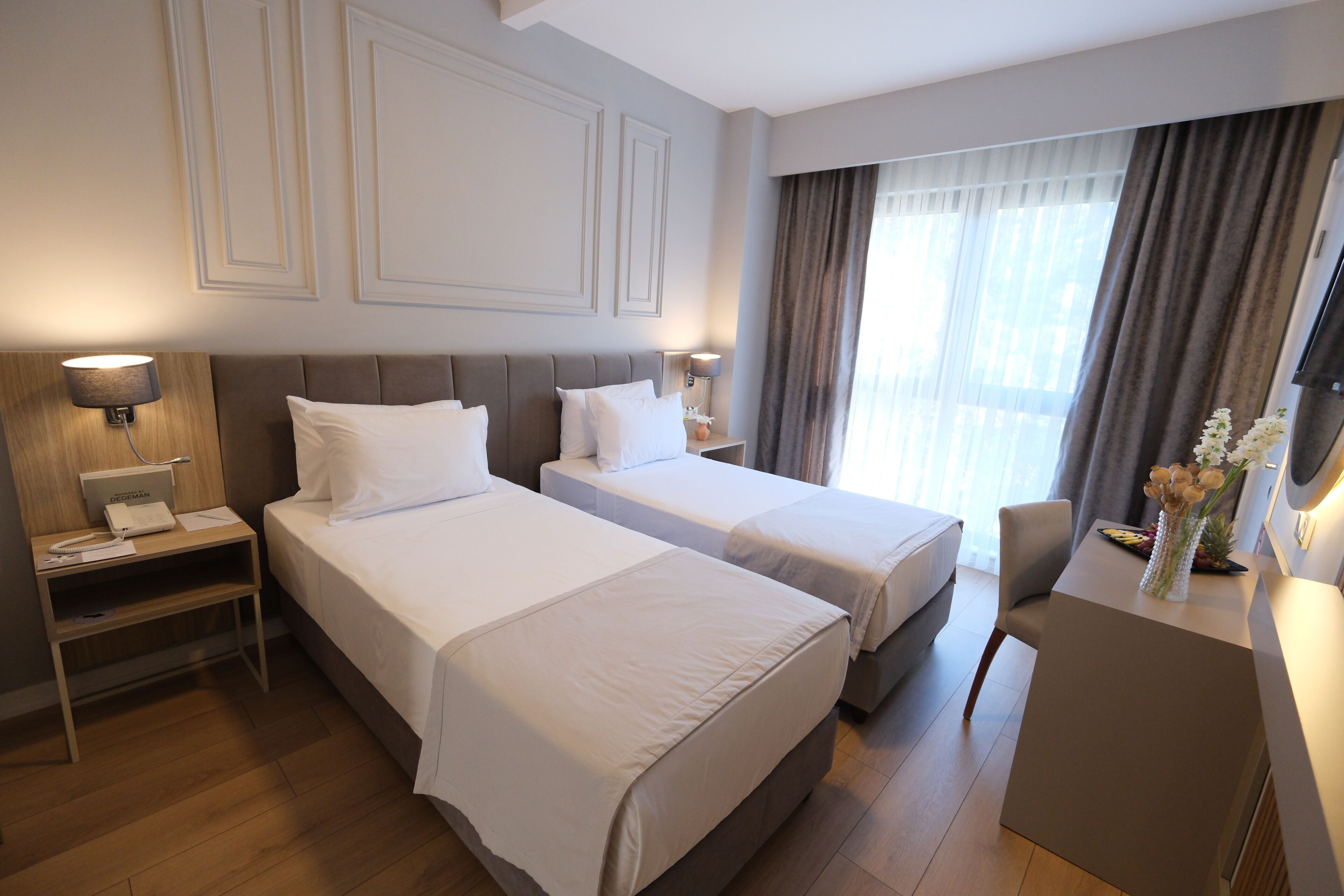 A hotel room with two beds, a desk, a chair, and a TV.