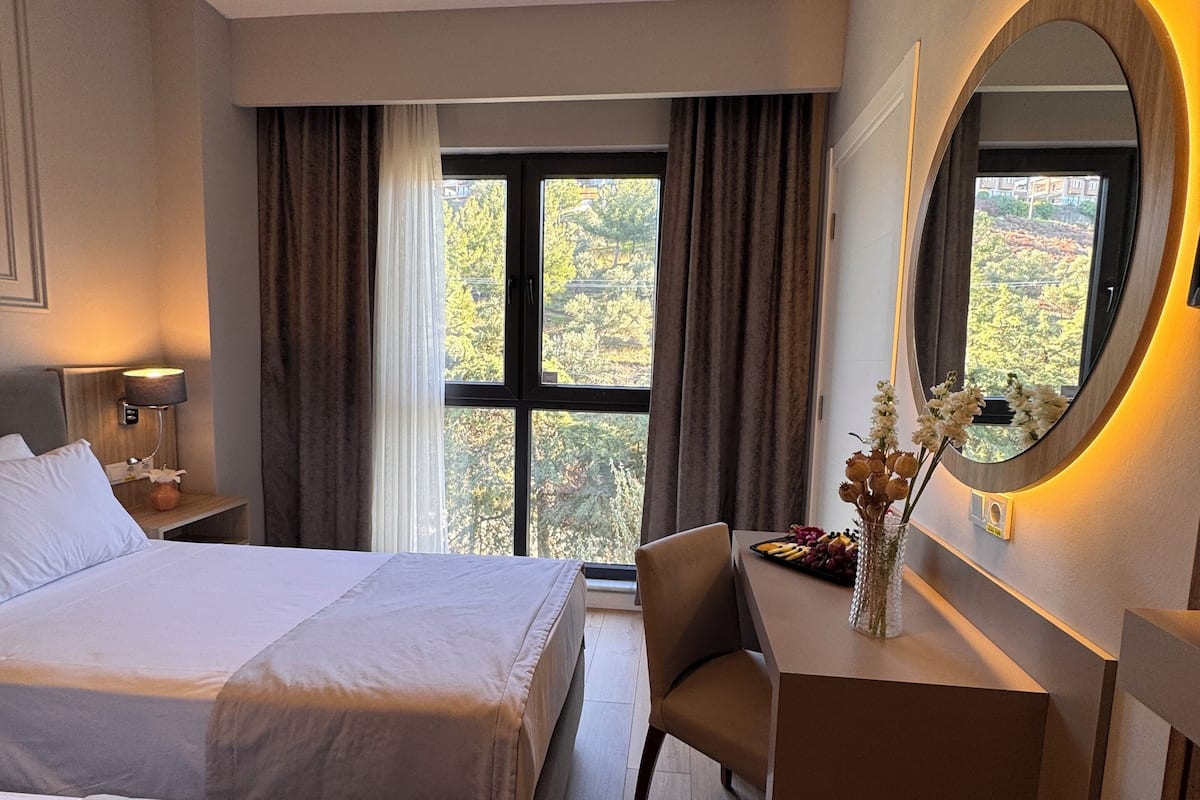 A hotel room with two beds, a desk, a chair, a mirror, and a window with curtains.
