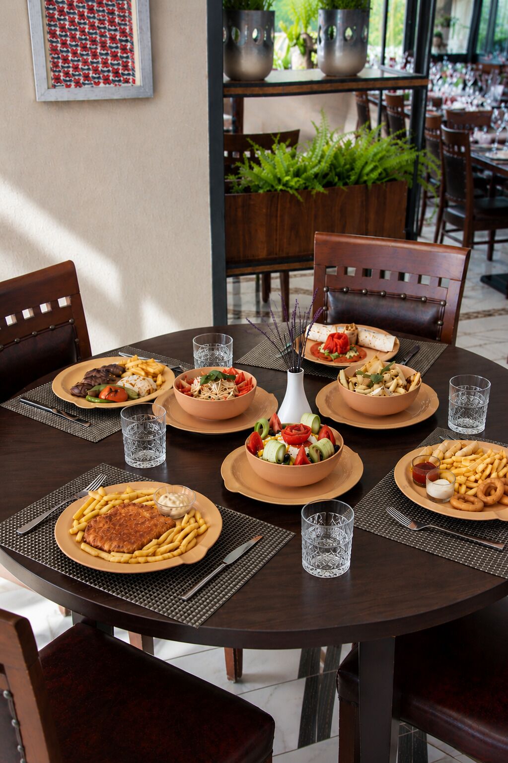 Una mesa de comedor con varios platos, incluyendo pasta, un bistec y una ensalada, sobre una mesa de madera oscura rodeada de sillas.