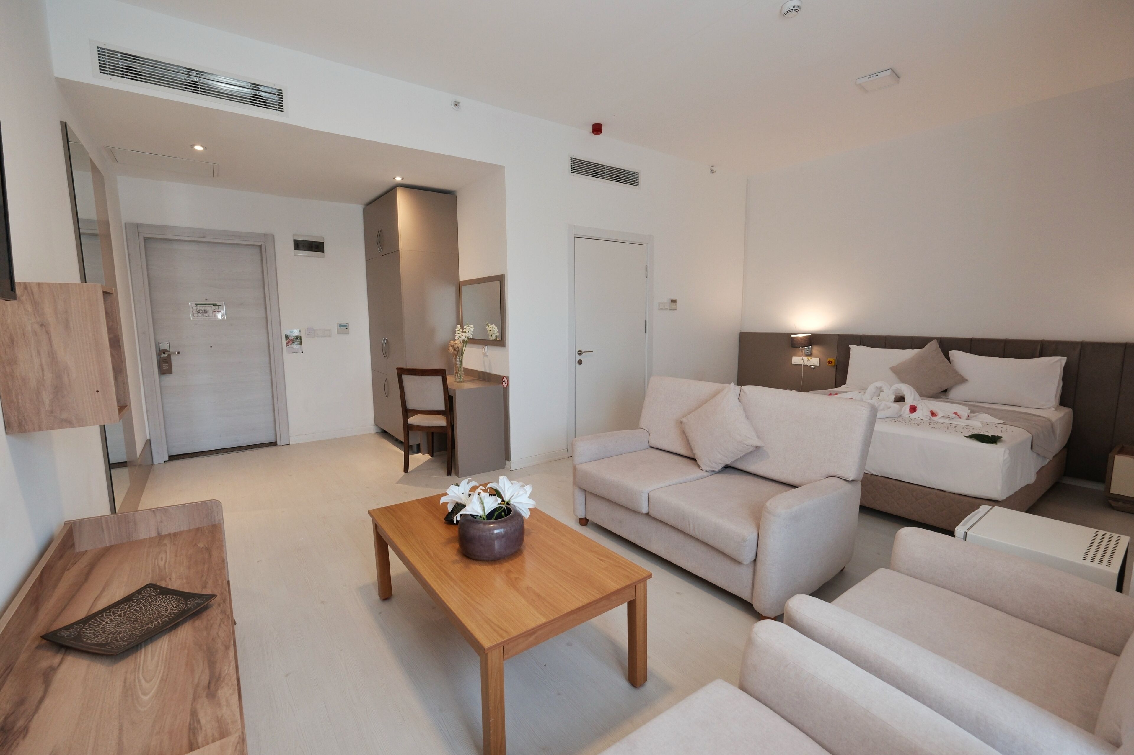 Una habitación de hotel moderna con una cama, un sofá, una mesa de centro de madera y una mesita con un florero.