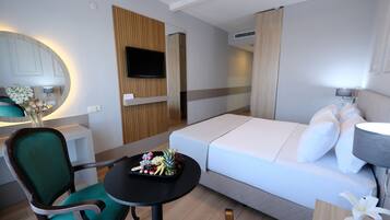 Et moderne hotelværelse med en seng, et lille bord med et frugtfad, en grøn stol, et fjernsyn ophængt på væggen og et spejl.