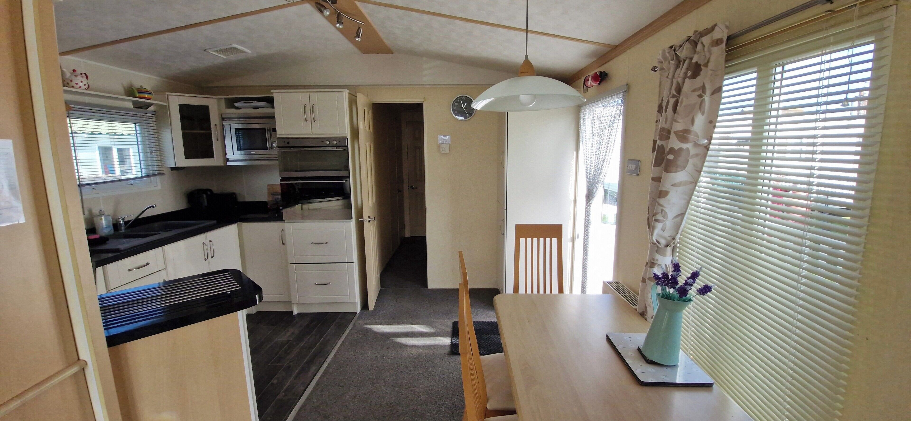 A compact kitchen with a microwave, oven, and cabinets. There is a dining table with a chair and a vase with flowers.