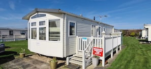 A mobile home with a designated parking area, a covered porch, and a visible window.