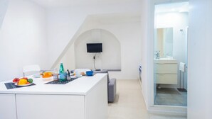 Een moderne keuken met een wit aanrecht, een flatscreen televisie aan de wand en een grijze bank.