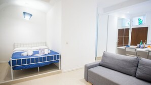Een slaapkamer met een bed, een grijze bank, een bureau en een spiegel.
