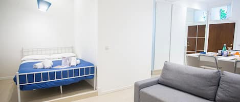 A bedroom with a bed, a grey sofa, a desk, and a mirror.