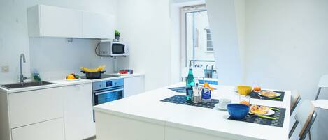 A modern kitchen with white cabinetry, a microwave, a stove, and a dining area with a table set for two.