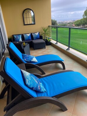 A balcony with two lounge chairs, a sofa, and a potted plant.