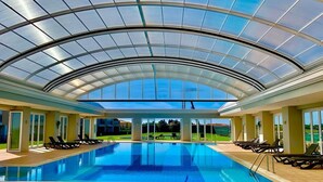 A large indoor swimming pool with a glass ceiling, surrounded by lounge chairs and a view of a green landscape. - Stunning bay views overlooking championship golf course (Lagos)