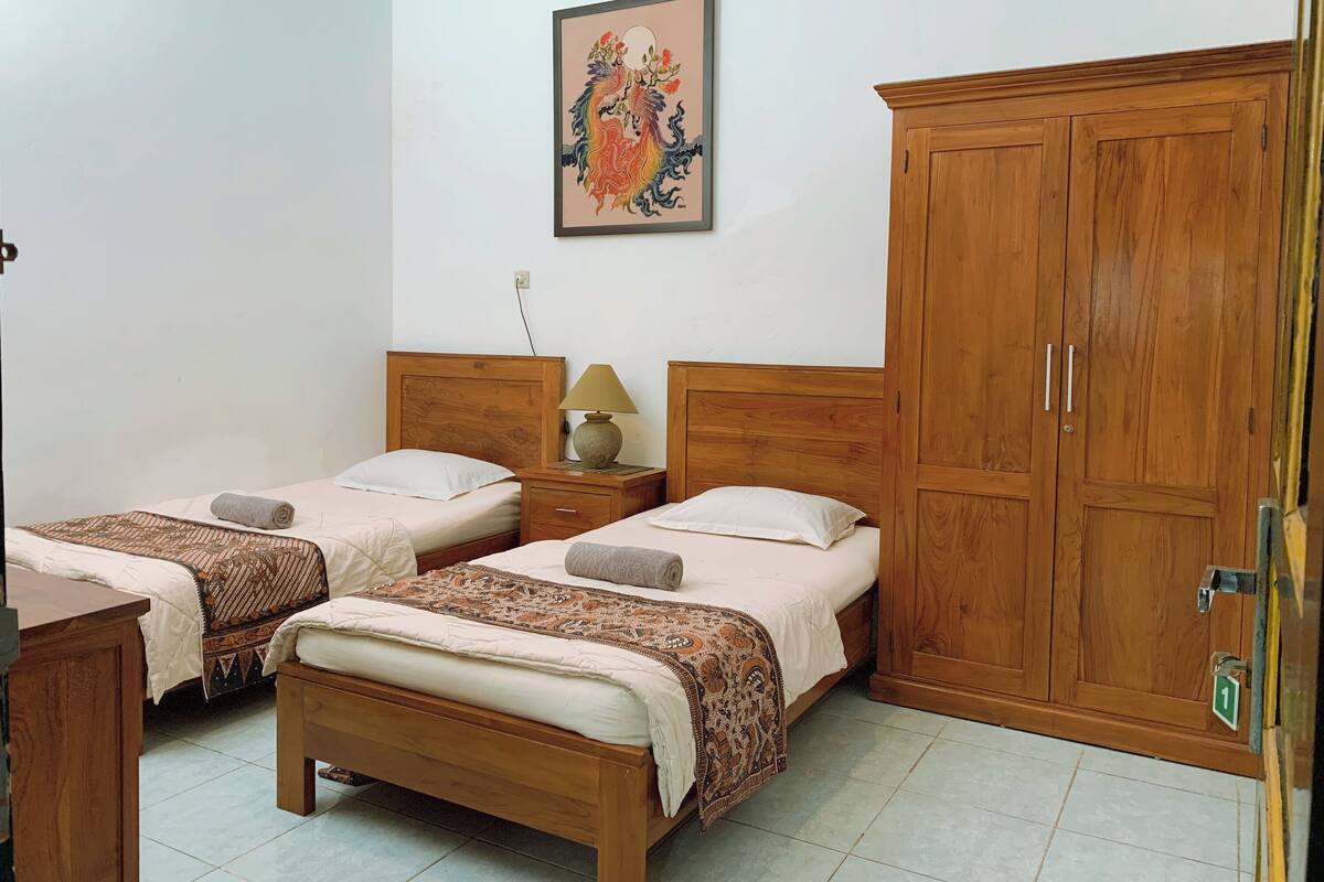 Una habitació amb dos llits de fusta, un armari de fusta, una meseta de nit amb una làmpada i un quadre penjat a la paret.