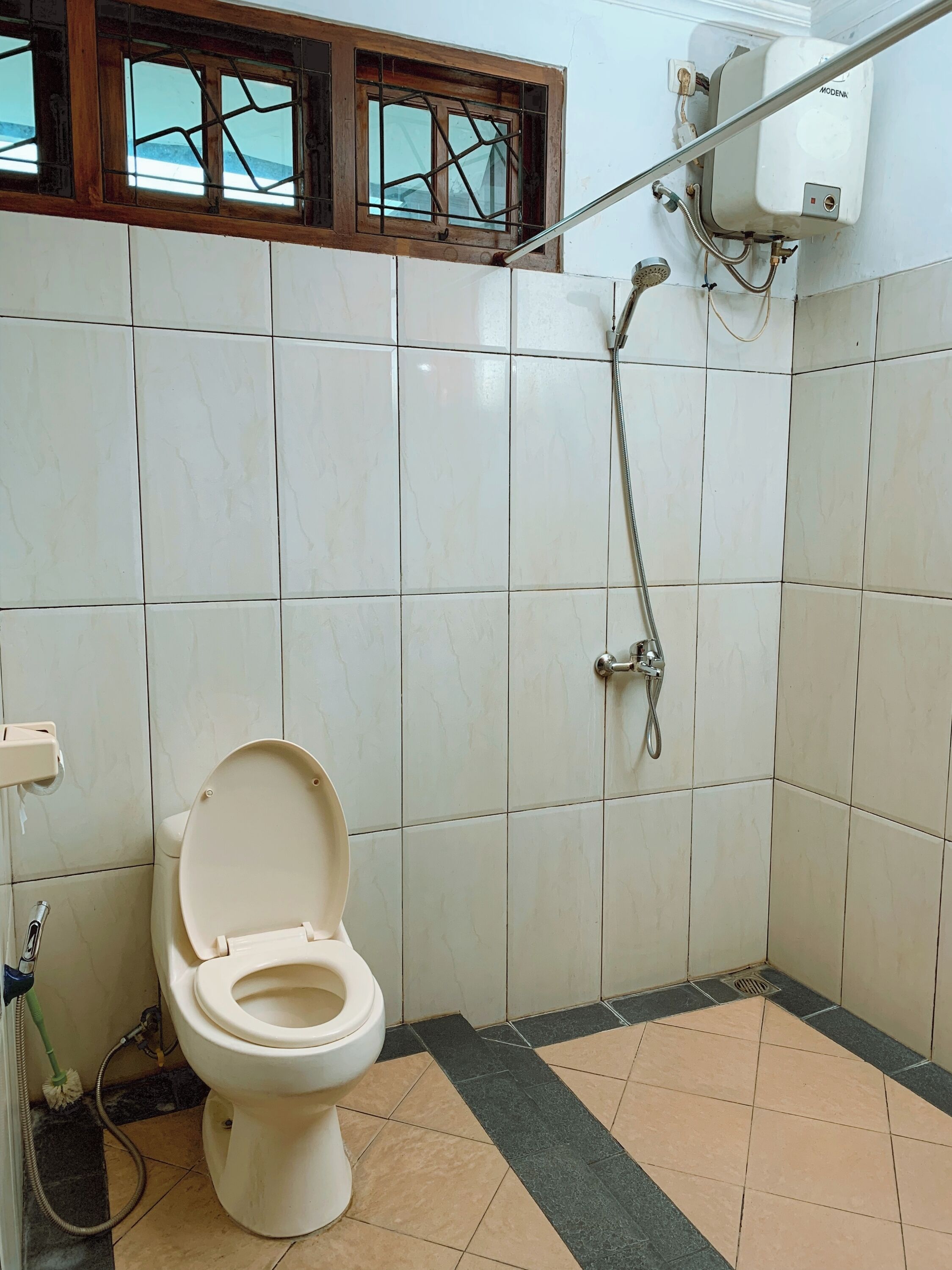 Een badkamer met toilet, douche en raam met houten kader.