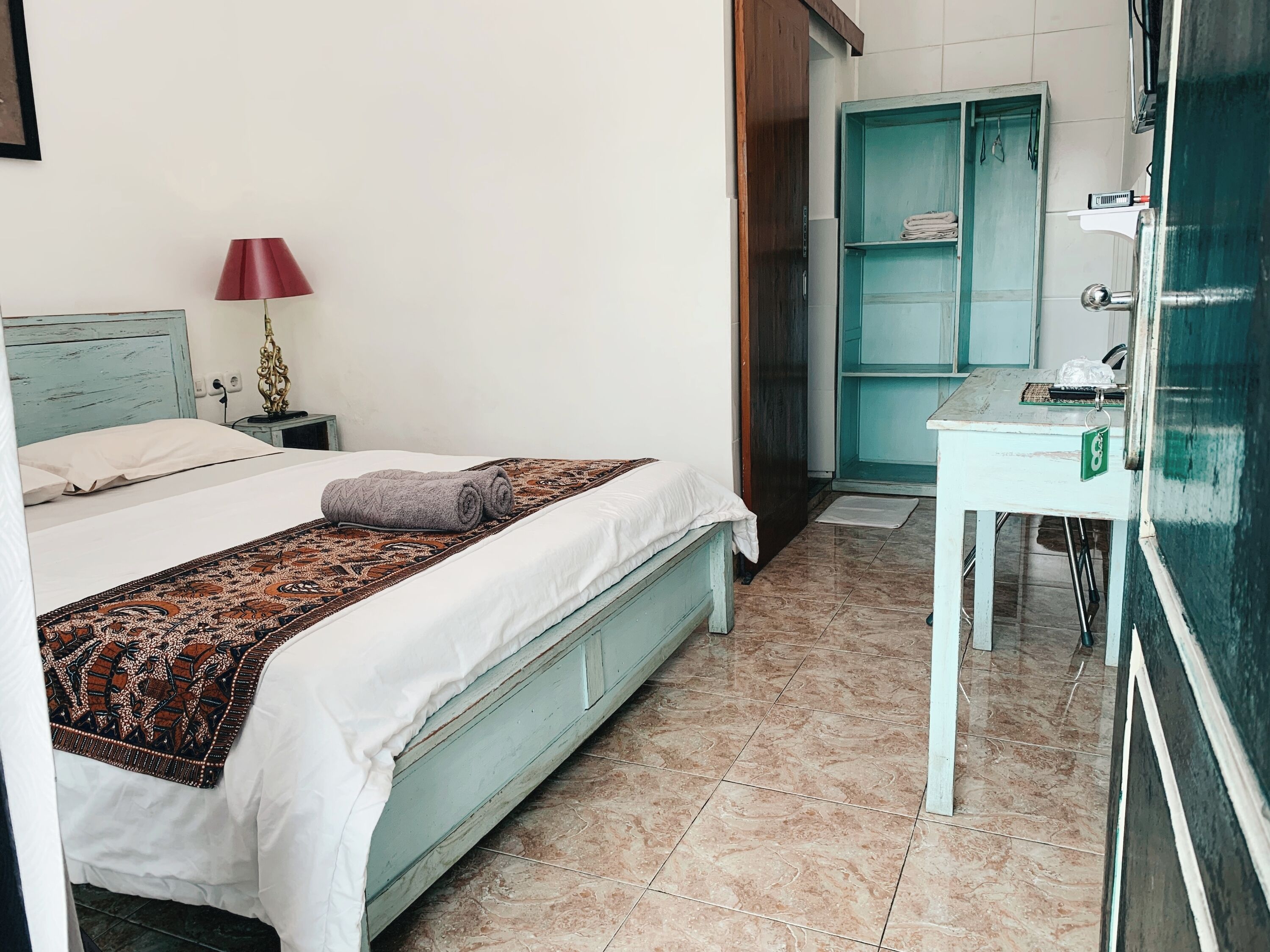 A bedroom with a bed, a nightstand, a lamp, a patterned blanket, and a bathroom with a sink and mirror.