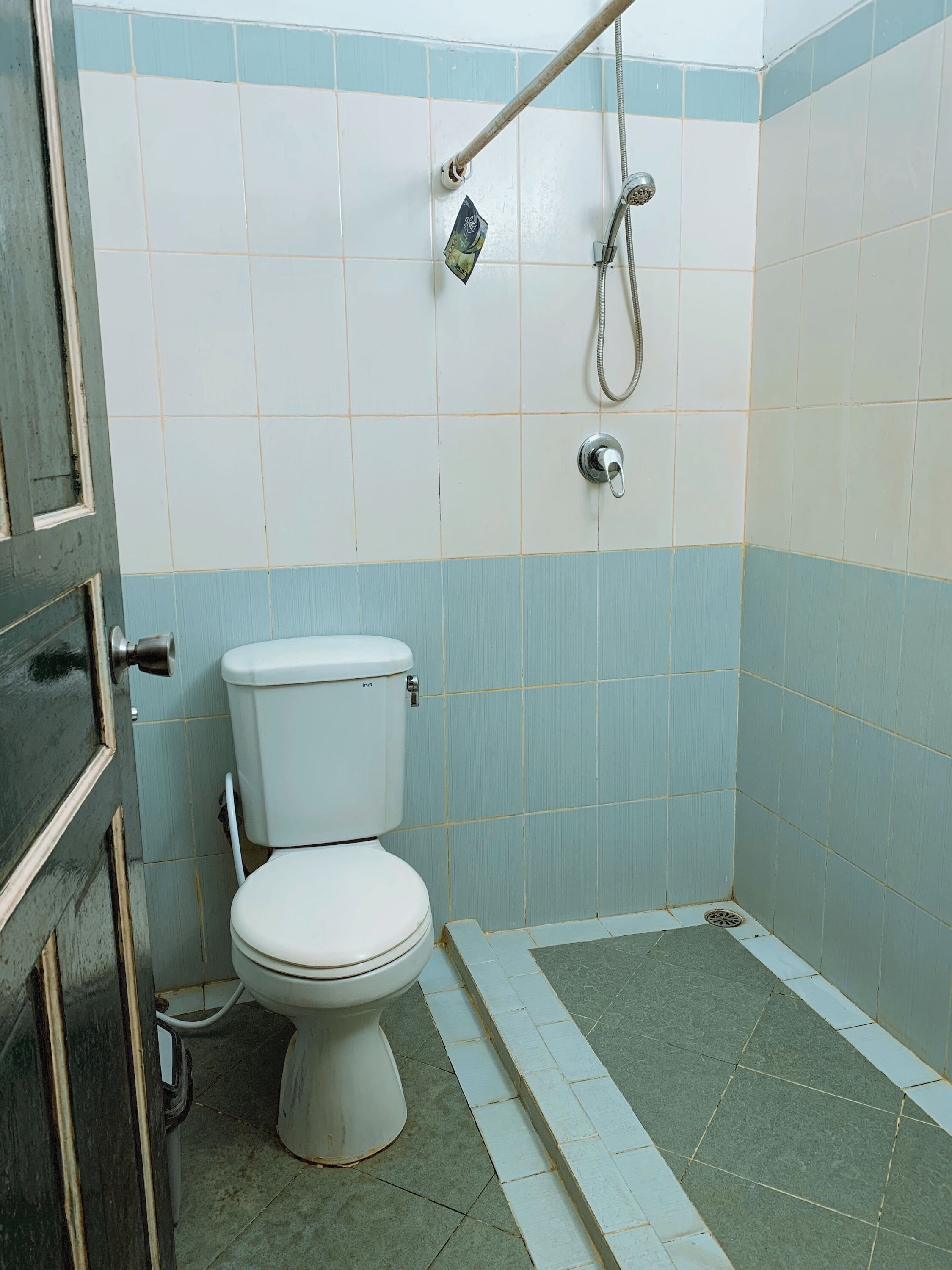 A small, basic bathroom with a toilet, a shower, and a door.