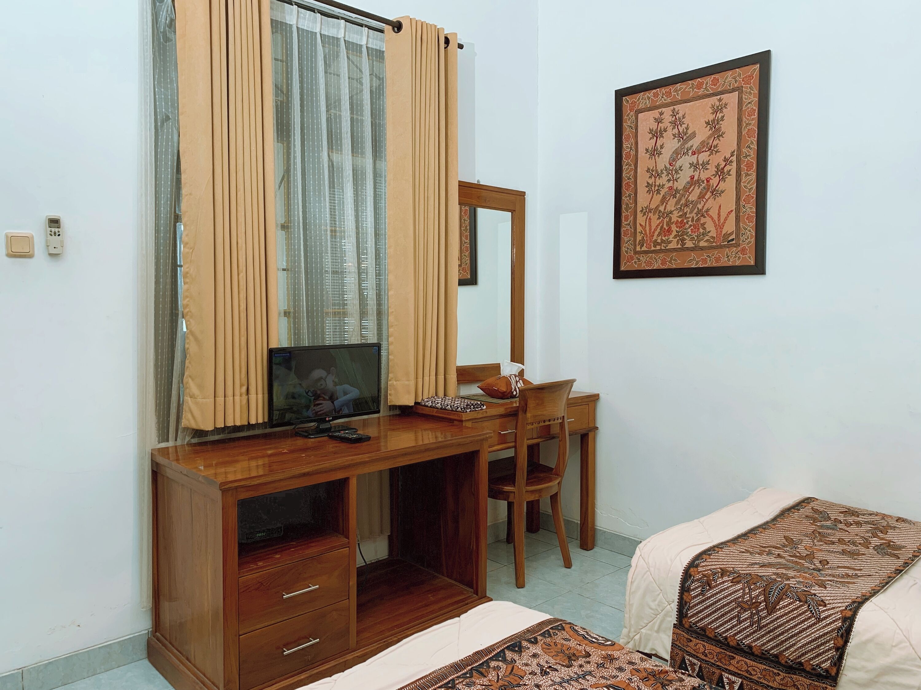 Una camera da letto con una scrivania in legno, una sedia, un letto con biancheria a motivi decorativi, uno specchio e un quadro appeso al muro.