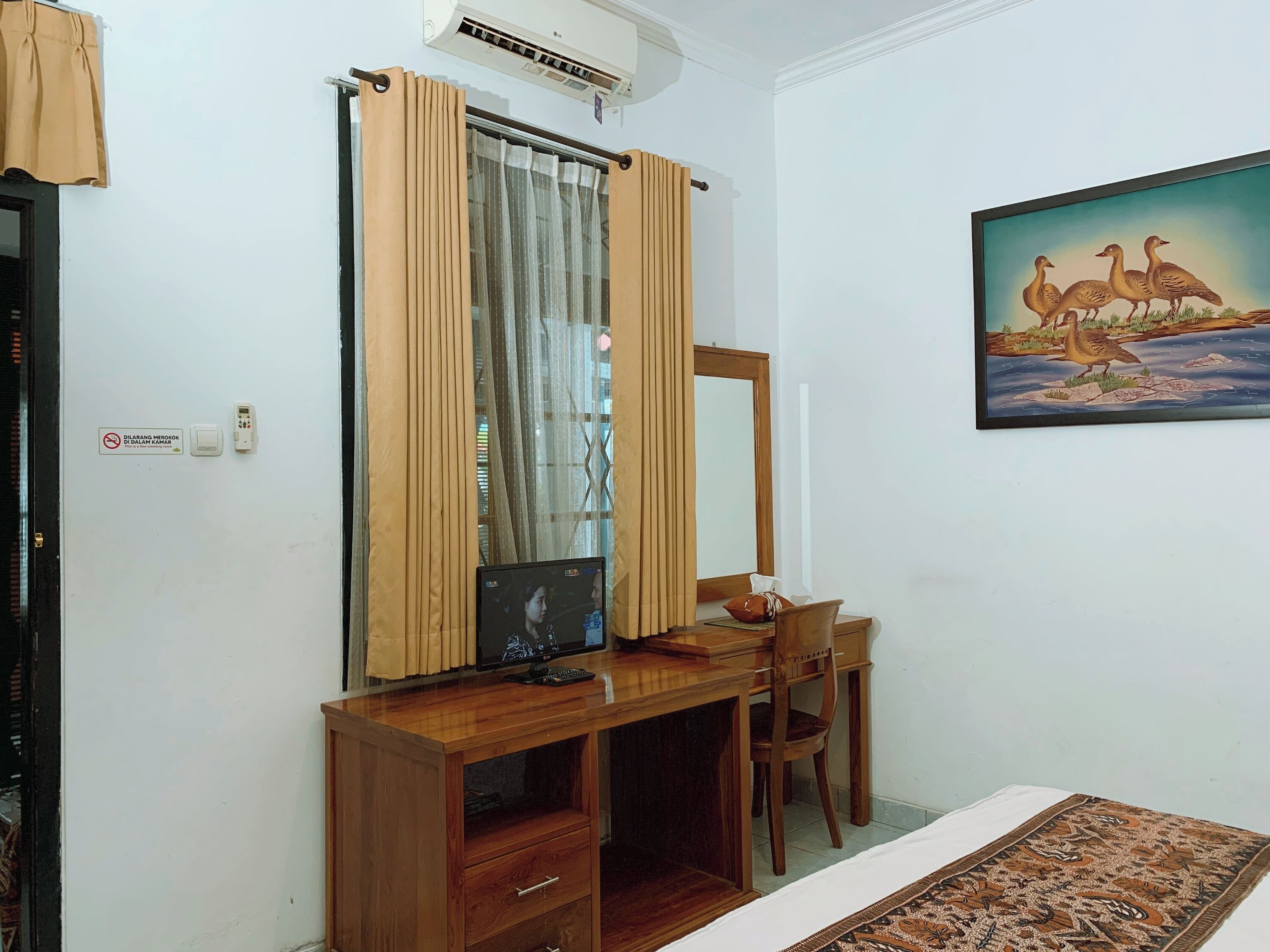 A room with a wooden desk, a chair, a television, a mirror, and a painting of ducks on the wall.