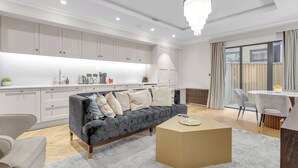 A modern kitchen with white cabinets, a grey sofa, and a dining area with a table and chairs.