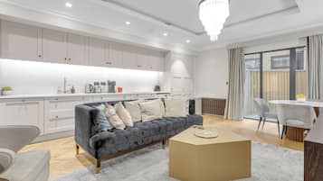 Una cocina moderna con armarios blancos, un sofá gris y un comedor con mesa y sillas.