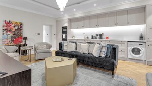 A modern living room with a sofa, a coffee table, a chandelier, and a washing machine in the background.