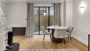 A modern living room with a round dining table, grey upholstered chairs, a black sofa, and a herringbone wood floor.