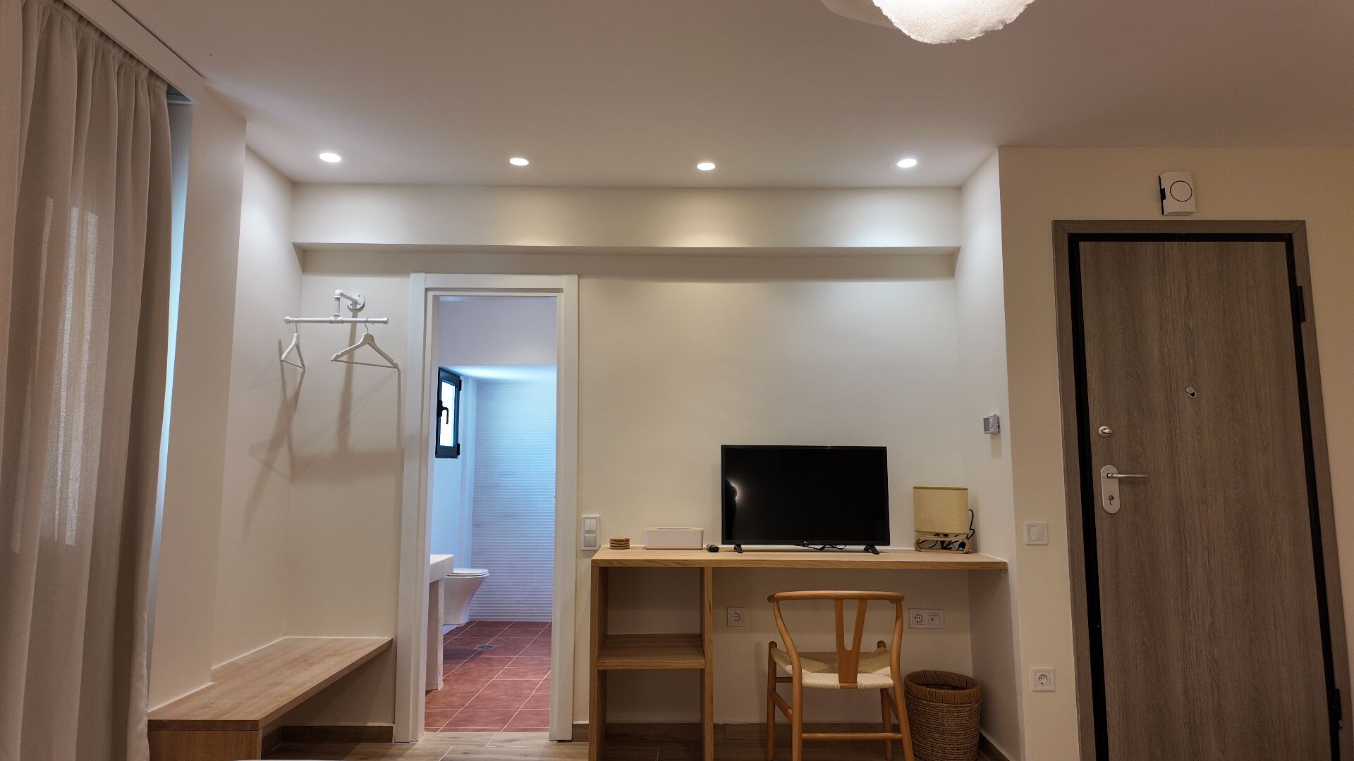 Een kleine kamer met een houten bureau, een televisie, een stoel en een deur.