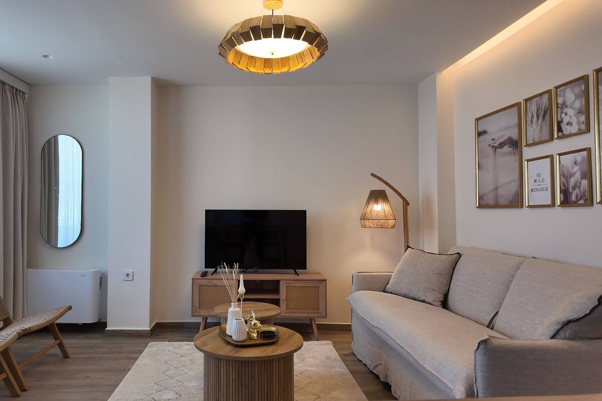A modern living room with a flat-screen TV, a sofa, a coffee table, and a large mirror.