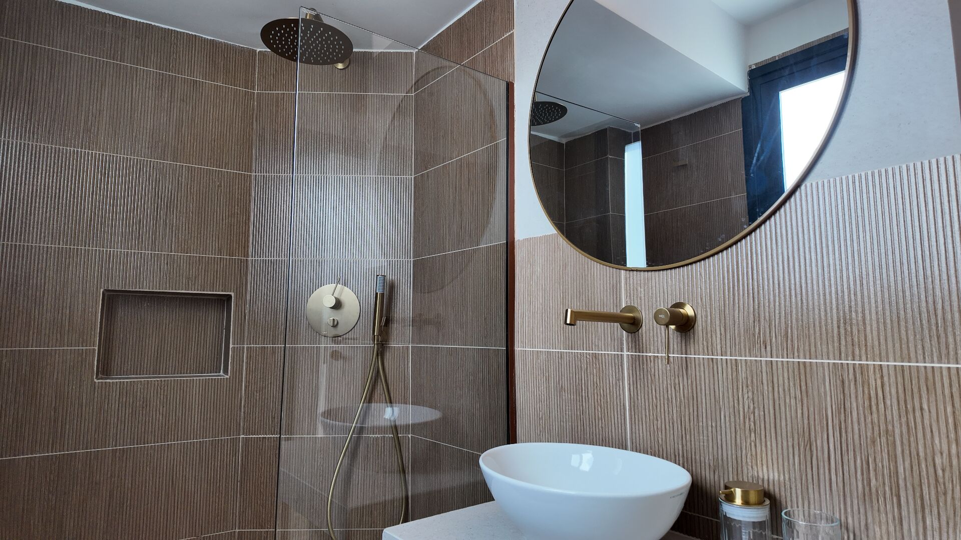 A modern bathroom with a large mirror, a round sink, and a shower with a handheld showerhead.