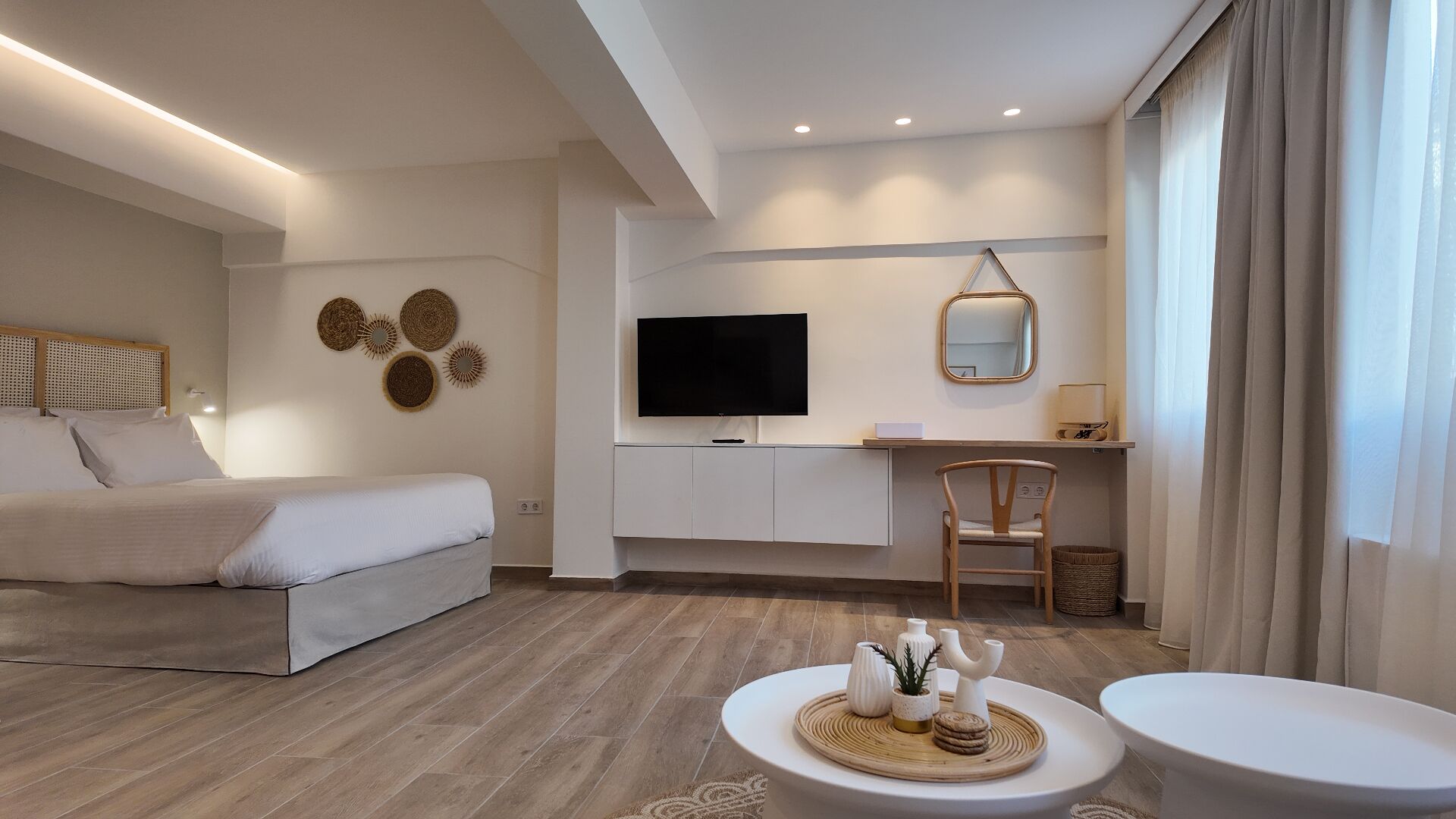 A modern hotel room with a bed, a desk with a TV, a chair, and a small table with decorative items.