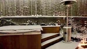 A snow-covered outdoor area with a wooden bench and steps leading up to a hot tub.