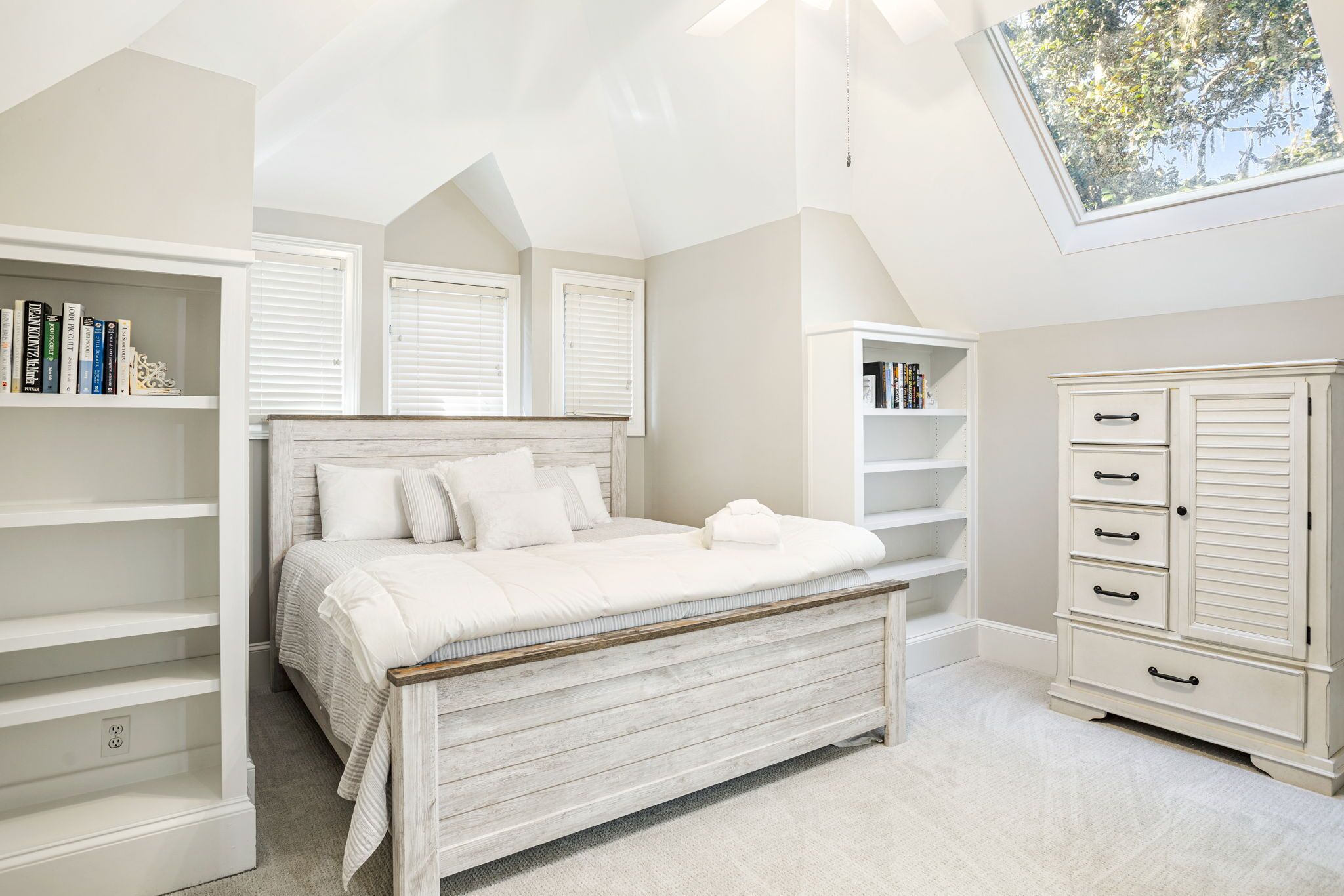 Een slaapkamer met een houten bed, witte kasten en een dakraam.