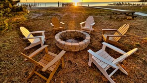 A beach scene with a fire pit surrounded by Adirondack chairs, a wooden bench, and a wooden walkway leading to the water. - All Year Retreat - Indoor Heated Pool, Beach, Game & Movie Cottage, Sleeps 21 (Hague)