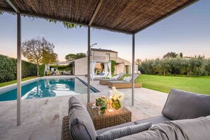 A covered outdoor area with a pool, seating, and a house in the background. - Villa Campanile Farmhouse (Castelfranco di Sotto)
