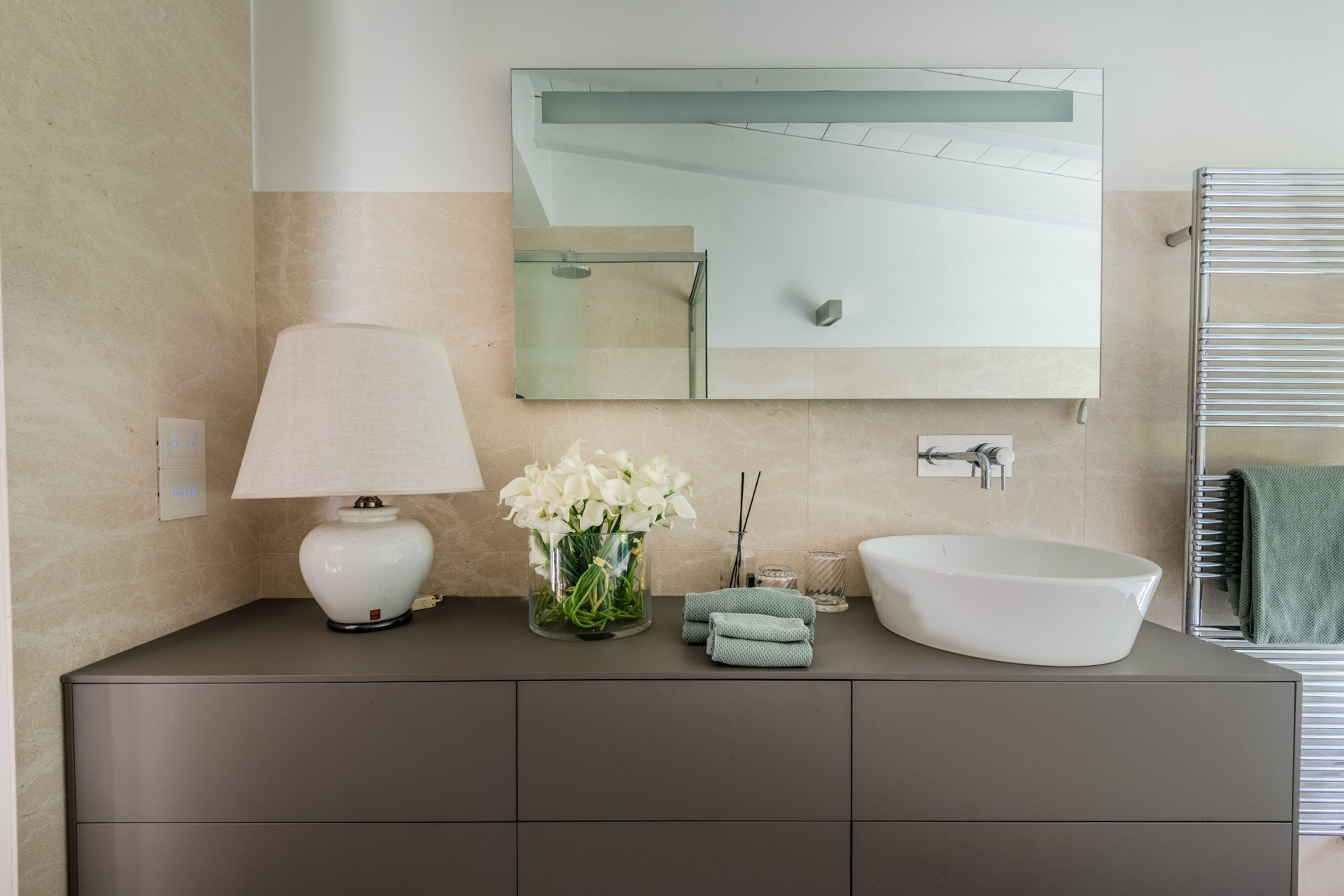 A modern bathroom with a large mirror, a white sink, a towel rack, and a lamp.