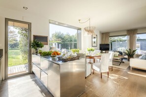 A modern kitchen with a central island, a dining area with white chairs, and a large window overlooking a garden. - Villa Campanile Farmhouse (Castelfranco di Sotto)