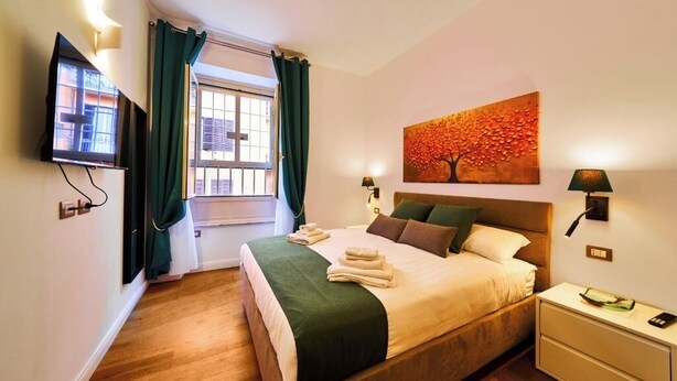 A hotel room with a bed, a TV, a painting, and a window with curtains.
