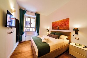 Una habitación de hotel con cama, televisión, un cuadro y ventana con cortinas.