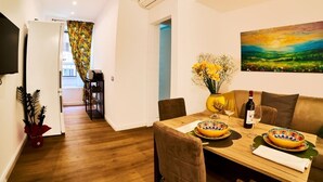 A dining area with a wooden table, chairs, a vase with flowers, and a painting on the wall.