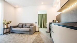 A modern living room with a grey sofa, a small side table with a vase, and a kitchen area with a countertop and cabinets. - Central Carol ApartHotel 1 (Bucharest)